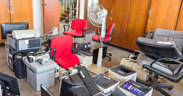 A cluttered office with old red and gray chairs among outdated electronics – What to do with old office chair? Office clearances can be a good opportunity to donate or recycle them.
